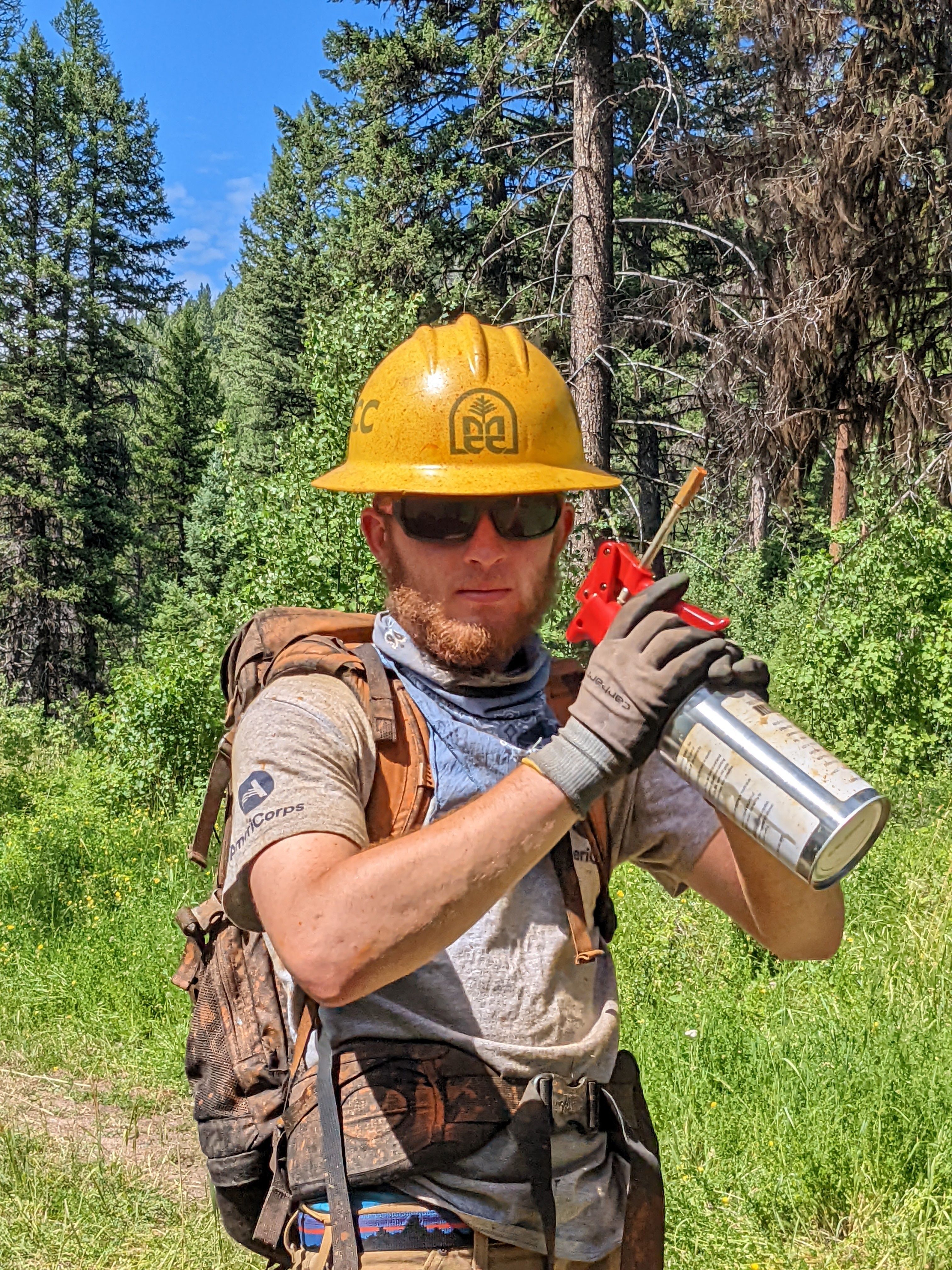 A crew member holds a spray paint can up to their face with a serious expression, as they get ready to mark some trees!