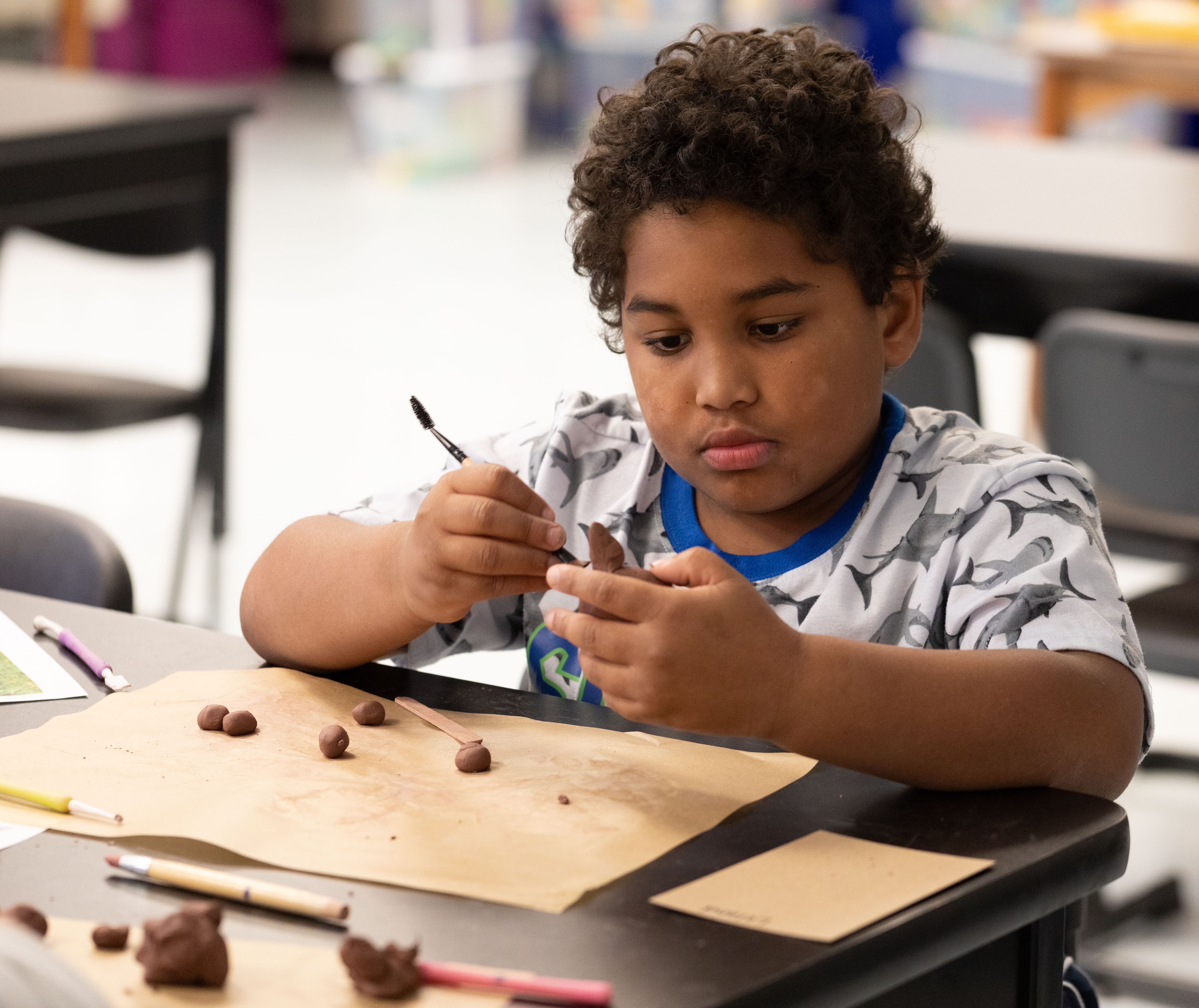 Boy sitting at his desk sculpting a red wolf from clay