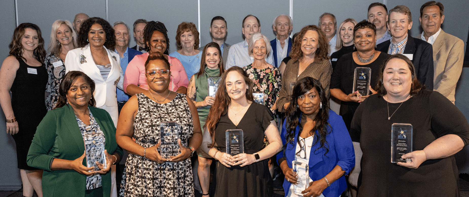 group of adults posing with awards on a stage