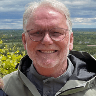 white man with gray hair and glasses smiles at the camera