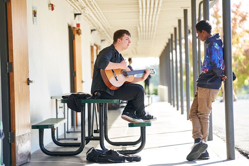 A student playing guitar for another student.