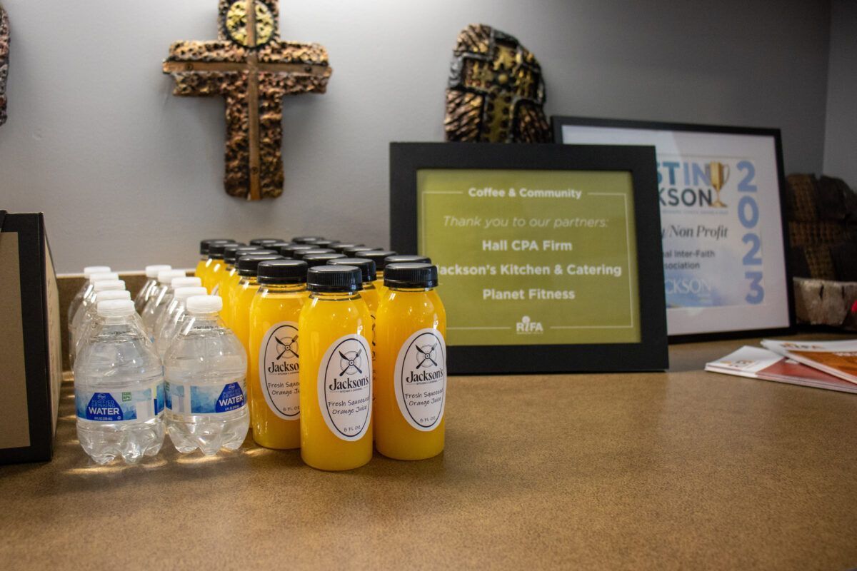 A tabletop with rows of water and orange juice bottles, and a framed thank-you sign.