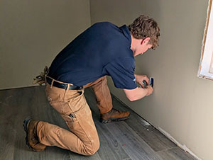 Volunteer kneeling to caulk or seal a wall corner near a window