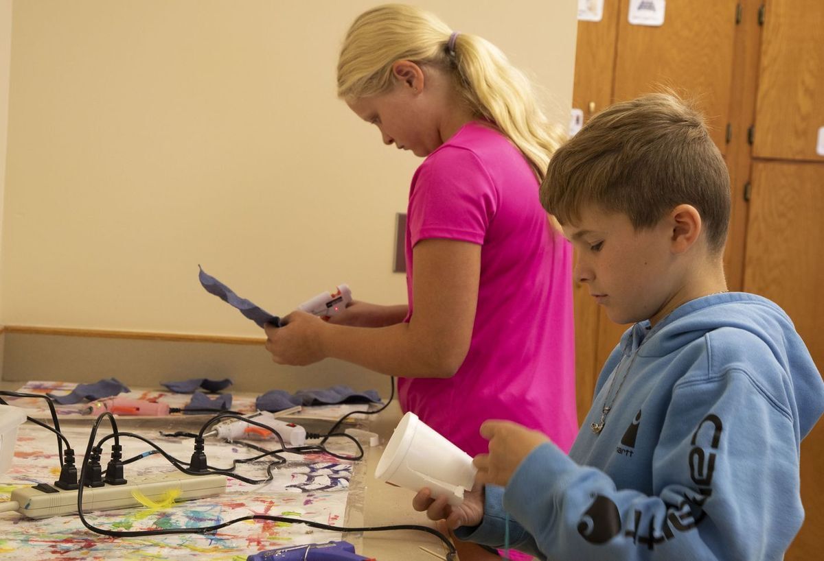 two students utilizing glue guns on an art project