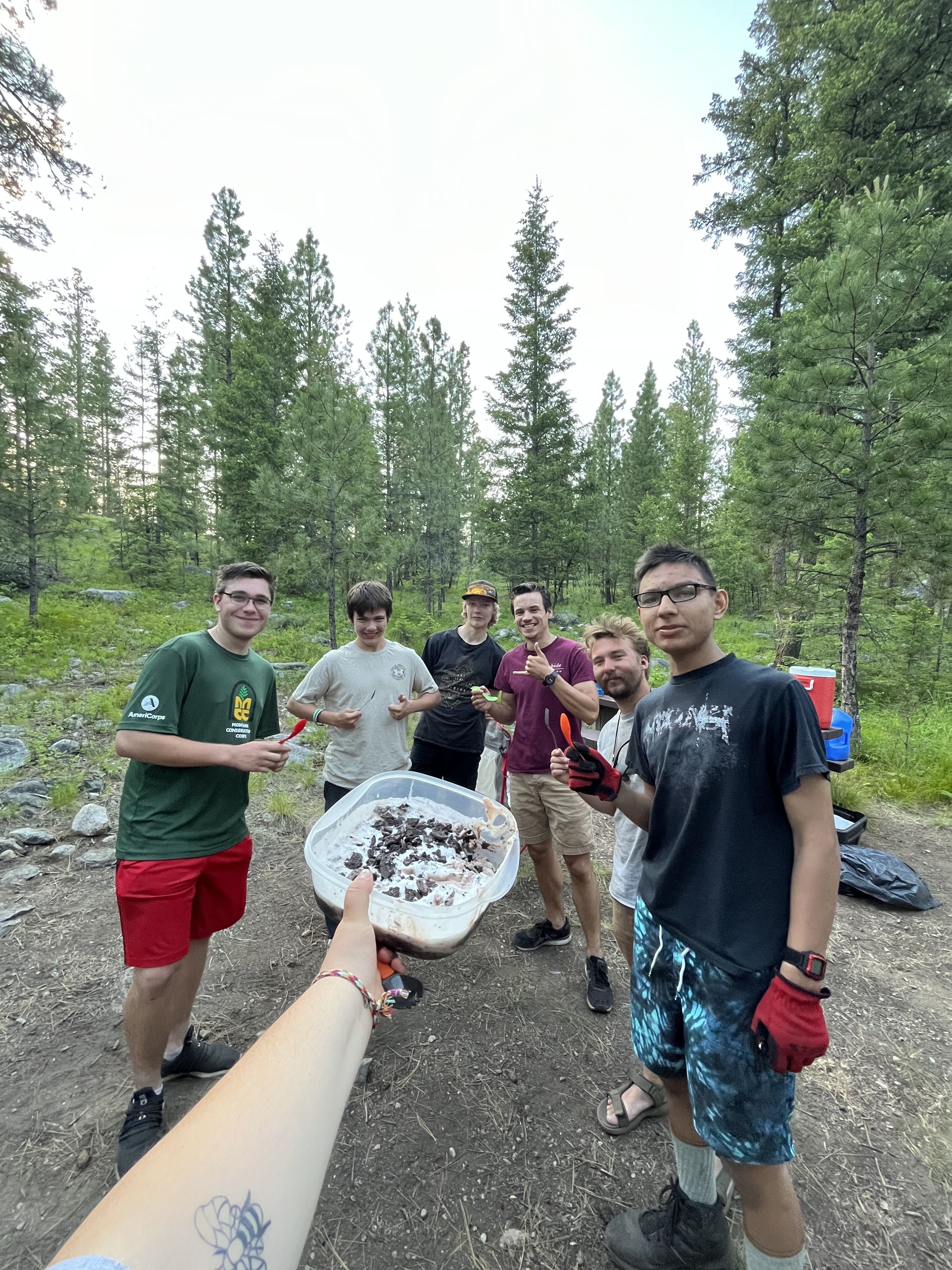 A crew stands smiling behind a tupperware filled with oreo dirt pie.