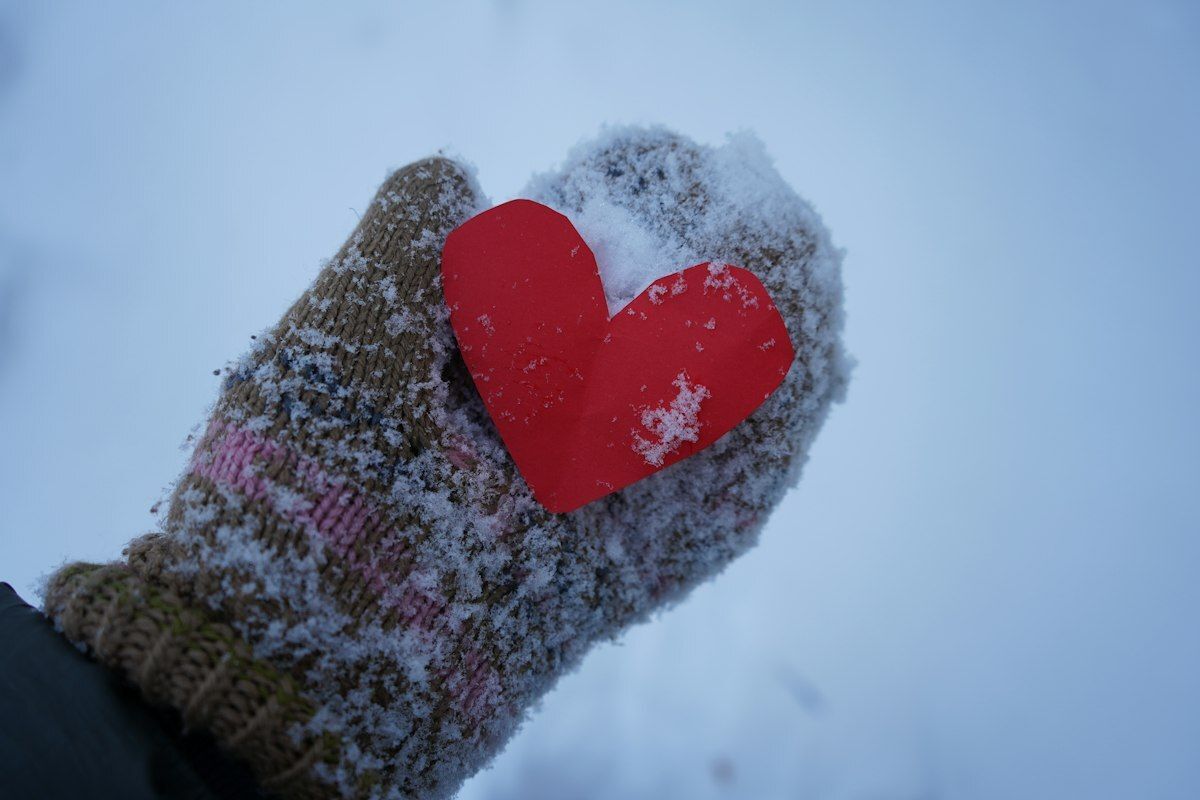 Snowy child's mitten holding a paper heart