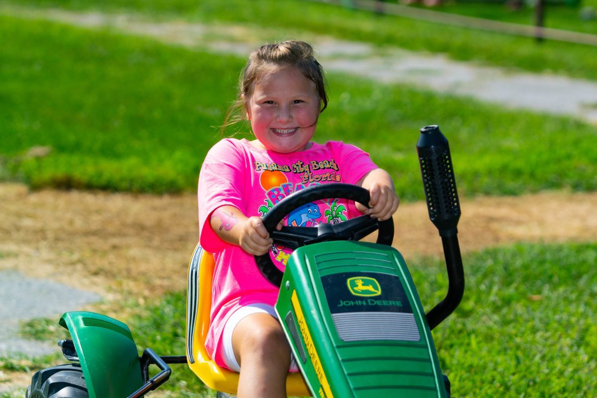 Girl driving green John Deer Pedal Tractor.