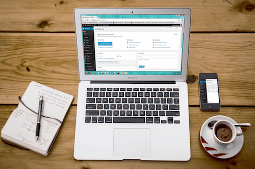 A laptop, coffee, and notebook sit on a desk.