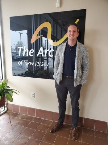 Michael Pearson Jr., the Director of the Children's Advocacy Program, in front of The Arc of NJ's yellow and orange logo.