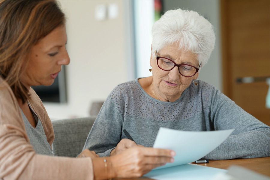 Professional, female, helping older woman will paperwork at kitchen table