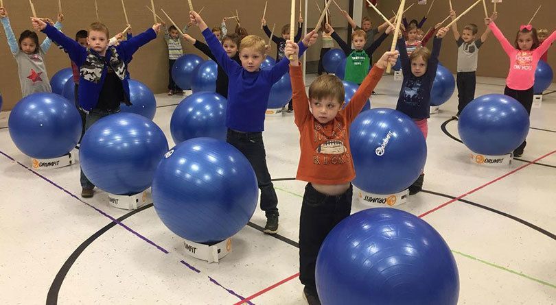 Kids standing in front of Blue exercise balls with their hands in the air and holding sticks.