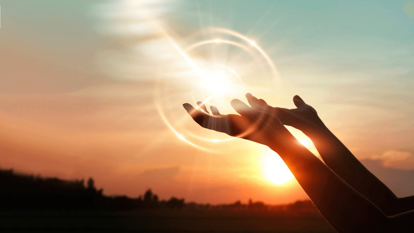 Two hands lifted up in prayer in front of a sunset sky background