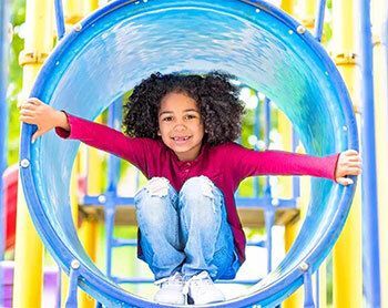 A child smiling in a blue playground tube slide.