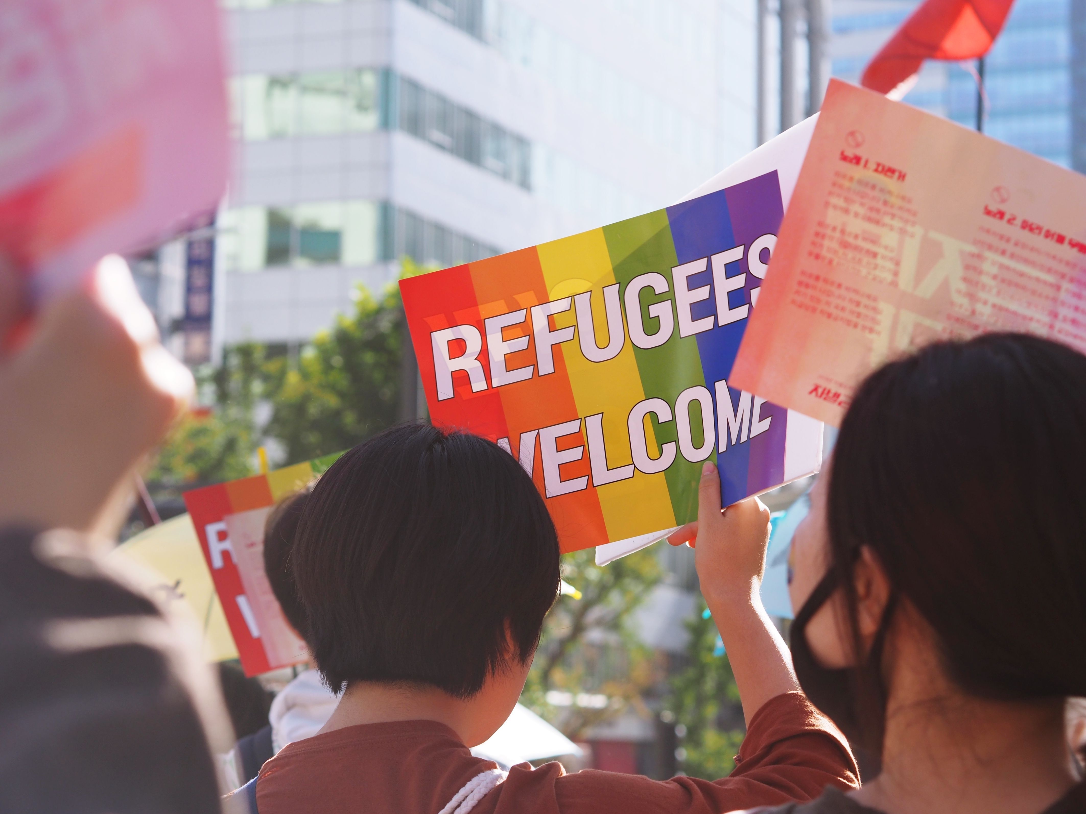 Photo Credit: Ra Dragon via Unsplash. Rainbow poster stating "Refugees Welcome"