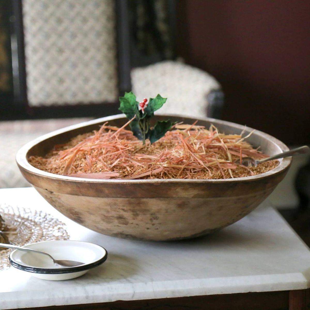 A wooden bowl with wood shavings and a sprig of holly.