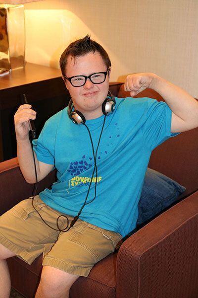 A person with glasses poses with headphones around their neck while sitting in an armchair.