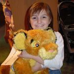 Young girl in white shirt smiling at camera and holding a Lion King stuffed animal