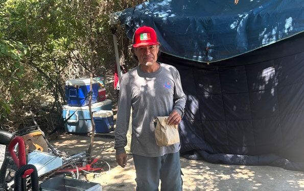Man standing in front of tent with a lunch sack