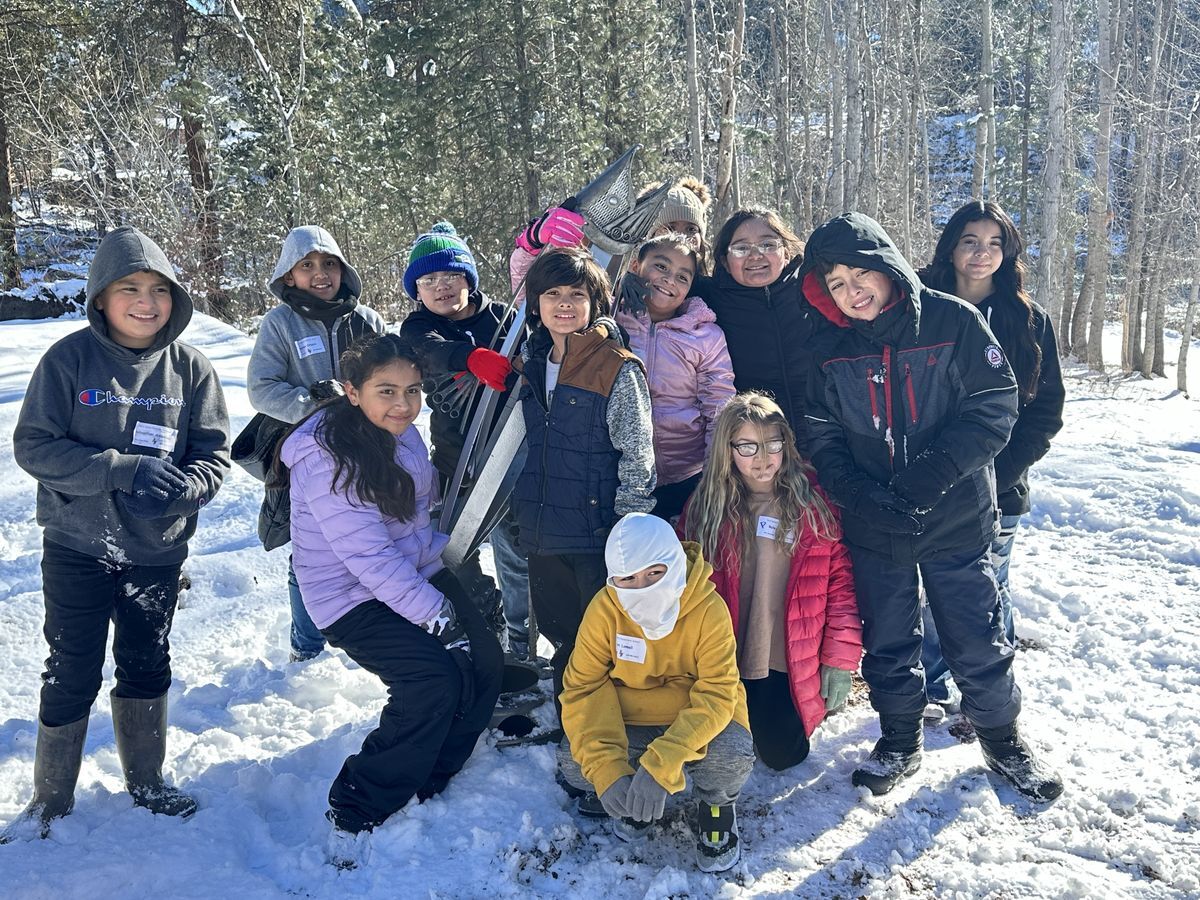 A group of students pose on snowshoes in a wintry scene by the river.