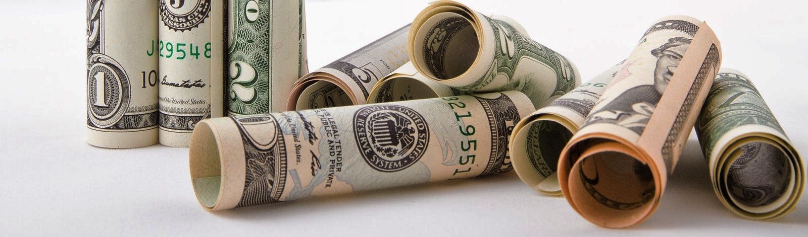 Photo of rolled up dollar bills in various denominations: 1, 2, 5, 20. Three rolled bills stand on the left in the background, while seven lay on their side in a pile on the right.