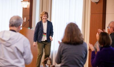 A woman, PSC Partners CEO Ricky Safer, steps down from a podium and smiles at a cheering audience