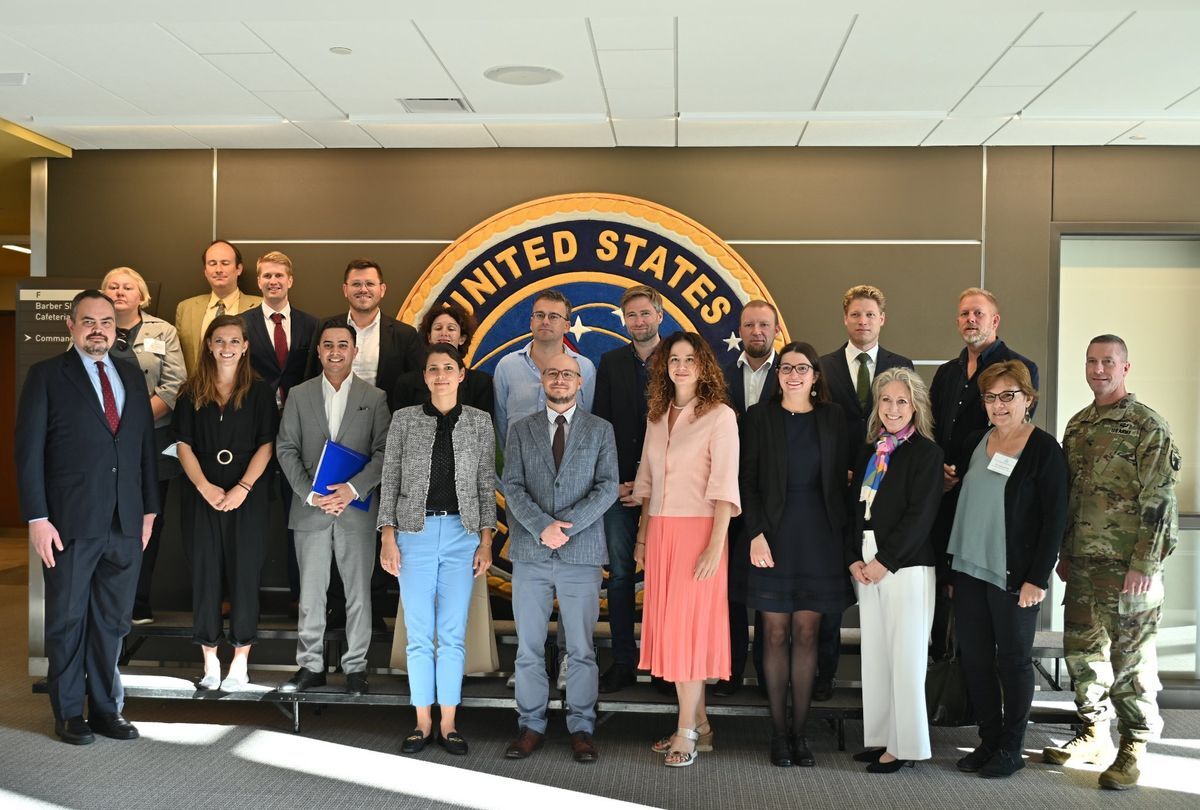 Group of people in business attire stand in front of the United States Seal.