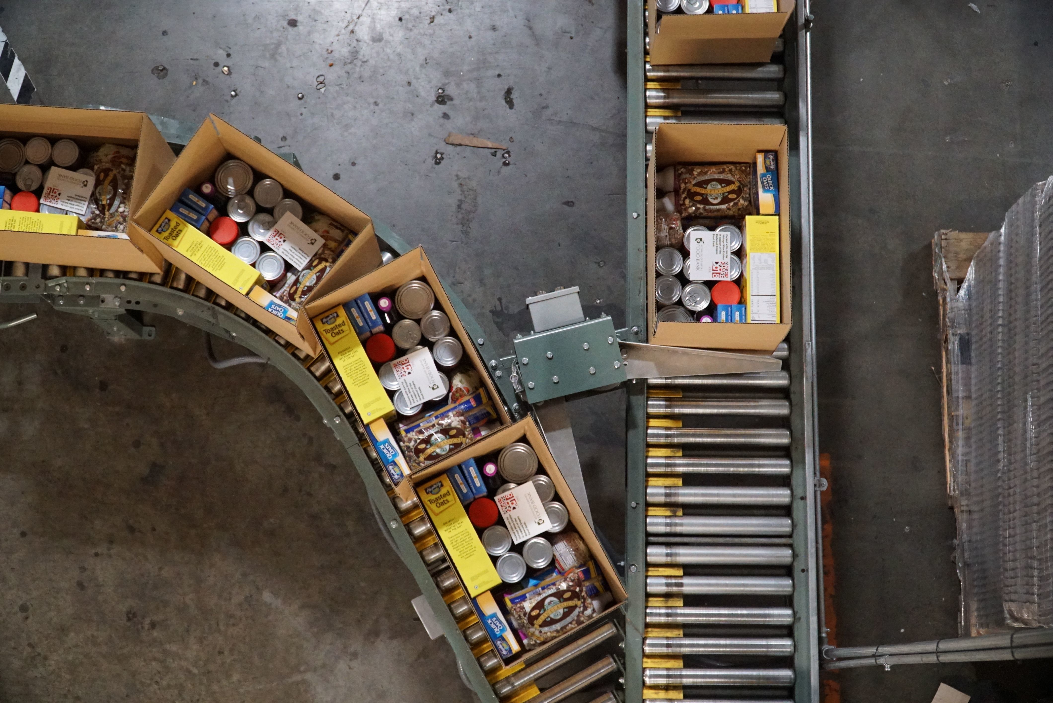 Overhead image of boxes being packed with food on a conveyor belt