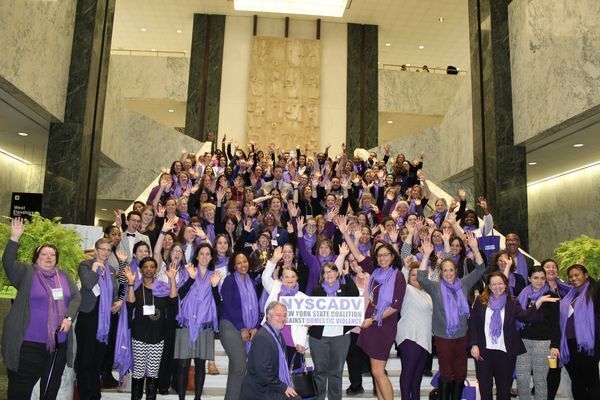 Group of Programs Members gathered together. They wear purple scarves and have hands raised.