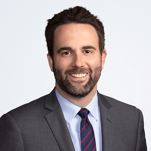 photo of Conor Dugan, who has dark hair and a beard and is wearing a suit