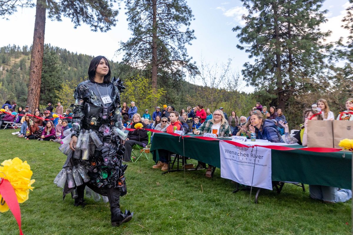 A photo of a person dressed in black with recycled materials on it strutting the runway.