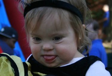 Toddler girl with Down syndrome in cheerleading costume at a past Buddy Walk event.