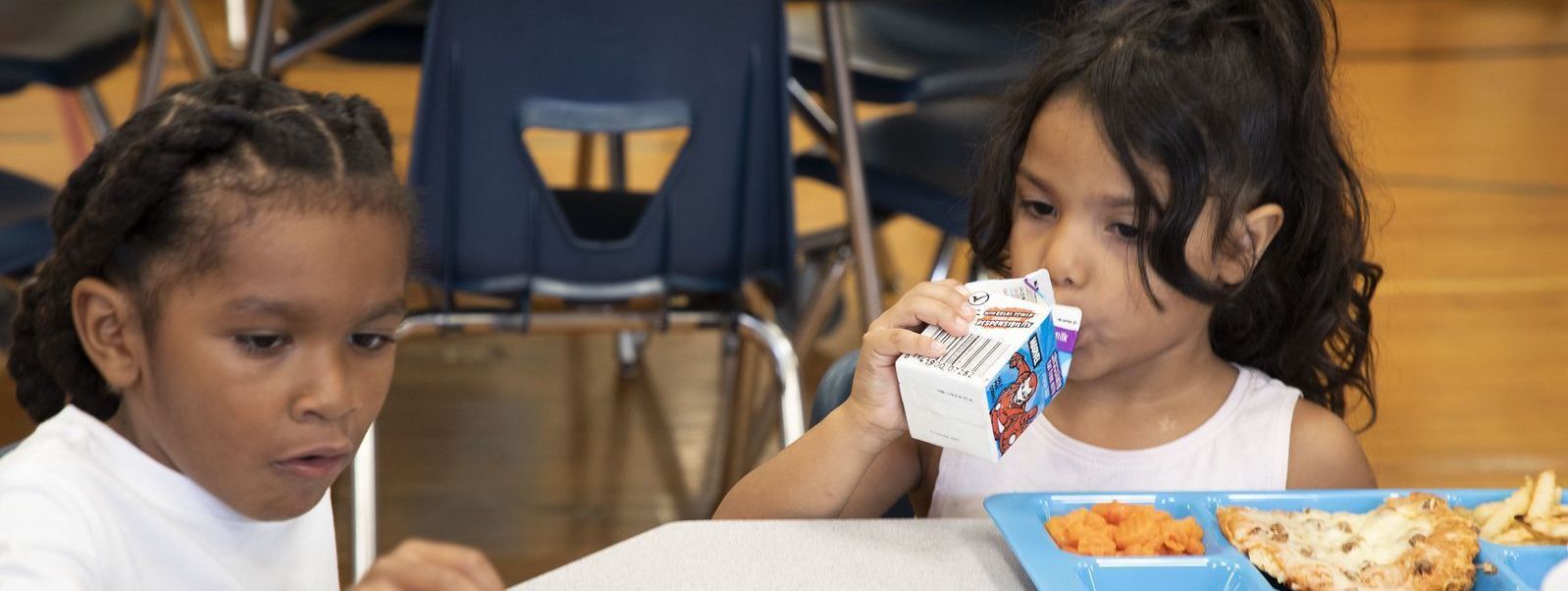 two elementary students eating lunch in a school cafeteria