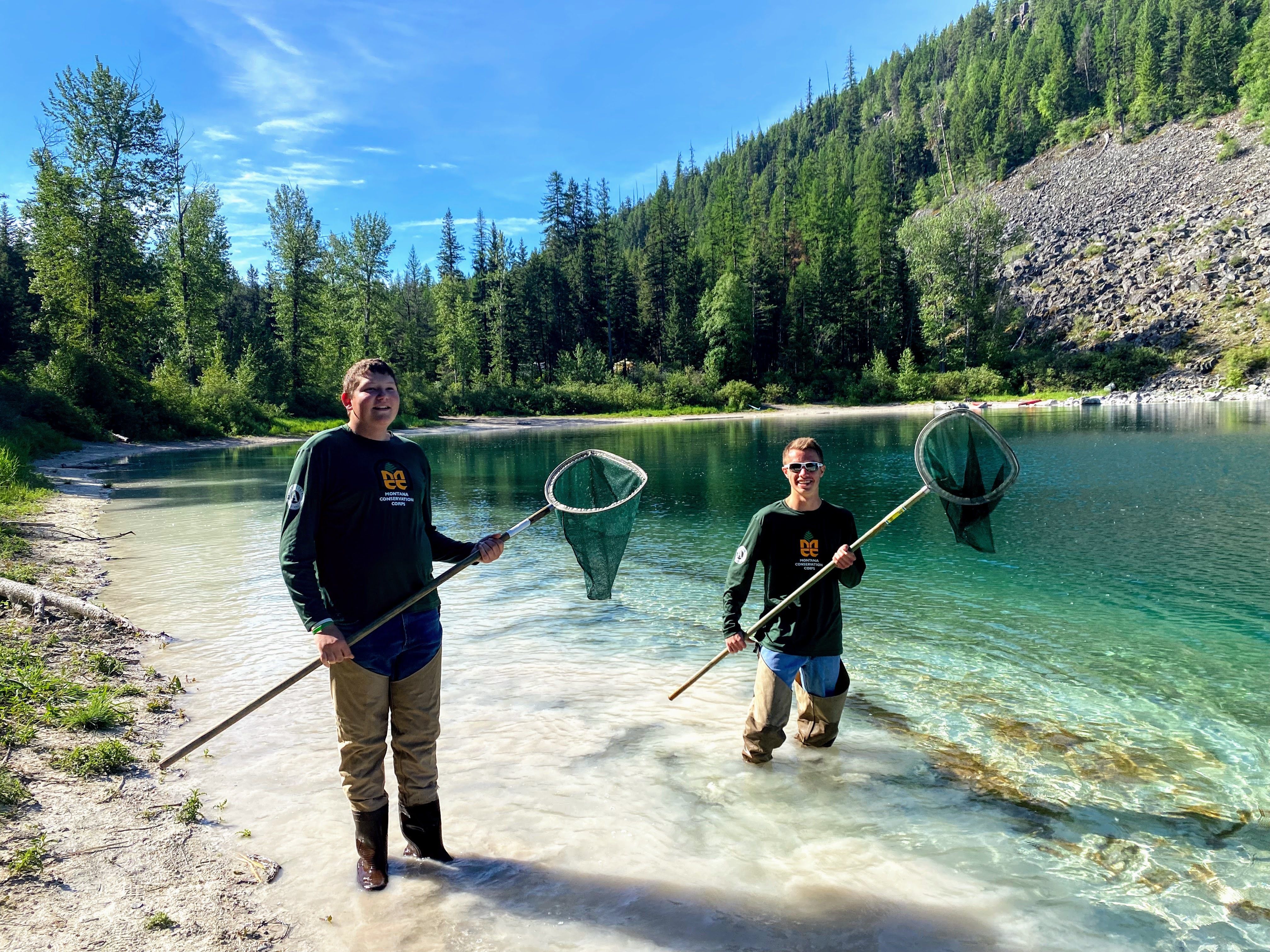 A youth member and a crew leader stand in a pond with nets