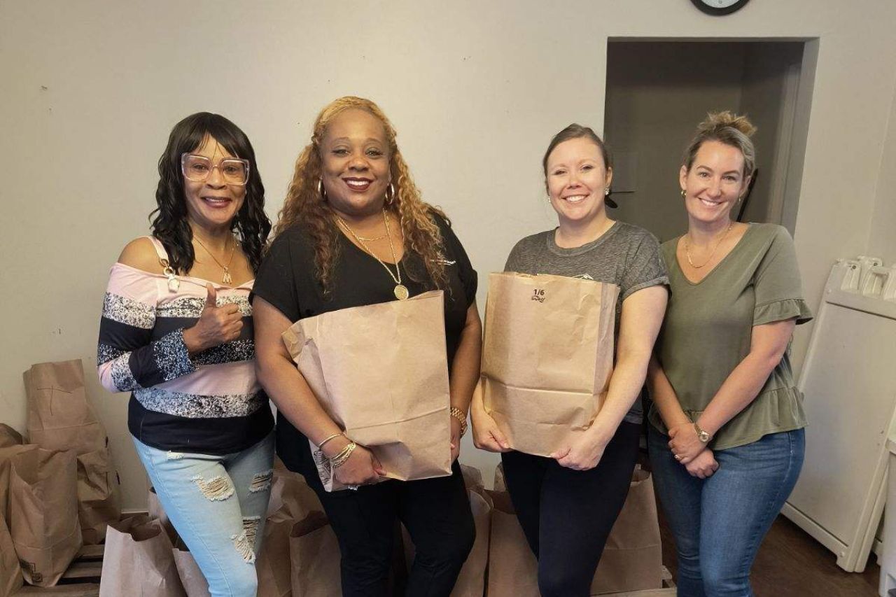 Four volunteers hold paper bags of groceries at the food pantry.