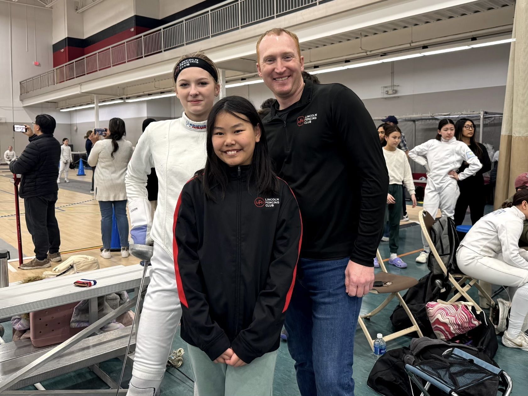 A coach poses with two youth fencers