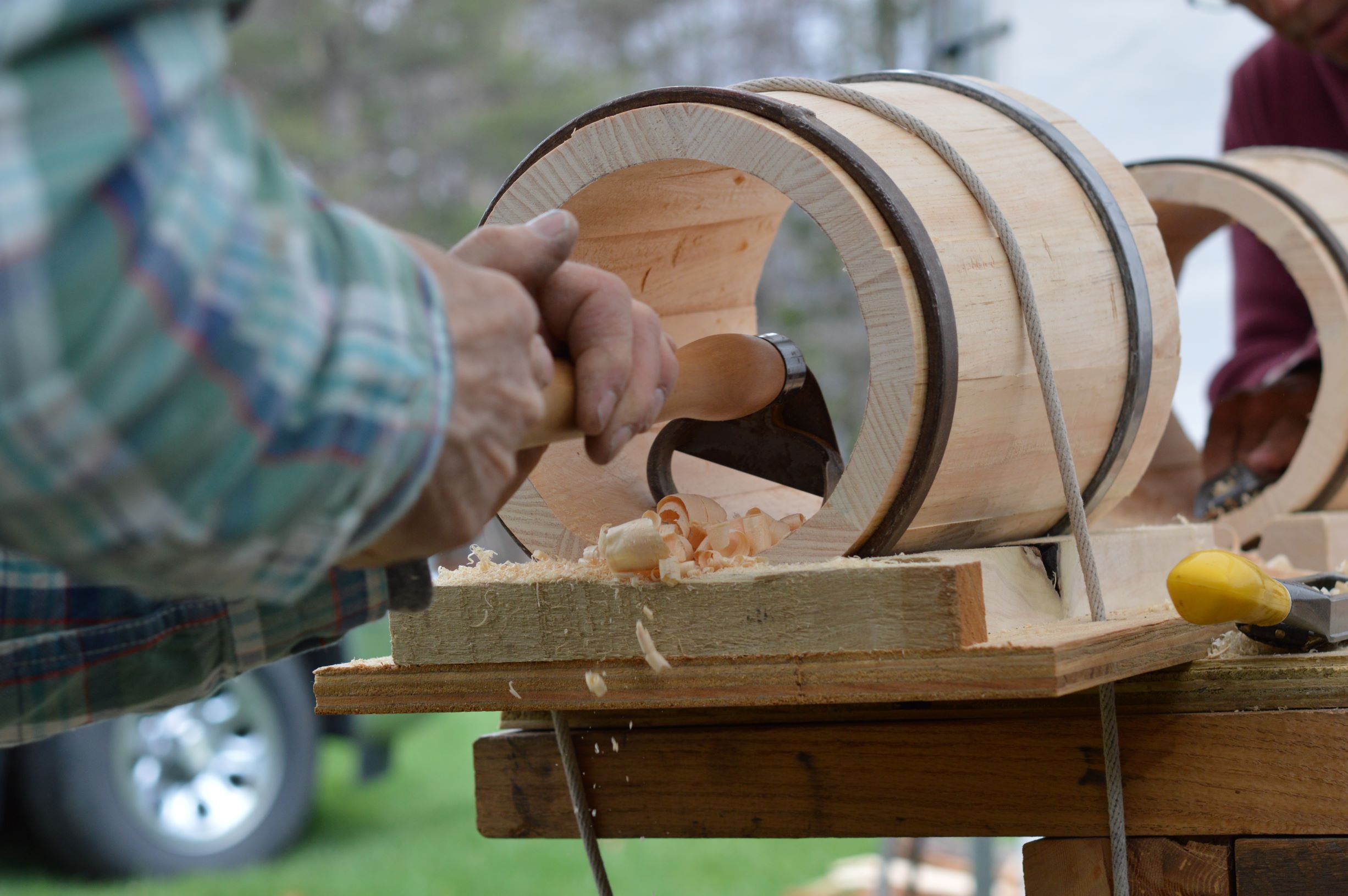 Close up image of hands using a cutting tool called a scorp to remove wood from the inside of a wooden bucket.