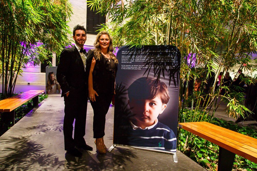 Tori and Mike Banu stand in front of a portrait of their son, Wils. They are in the atrium of the Cleveland Museum of Art.