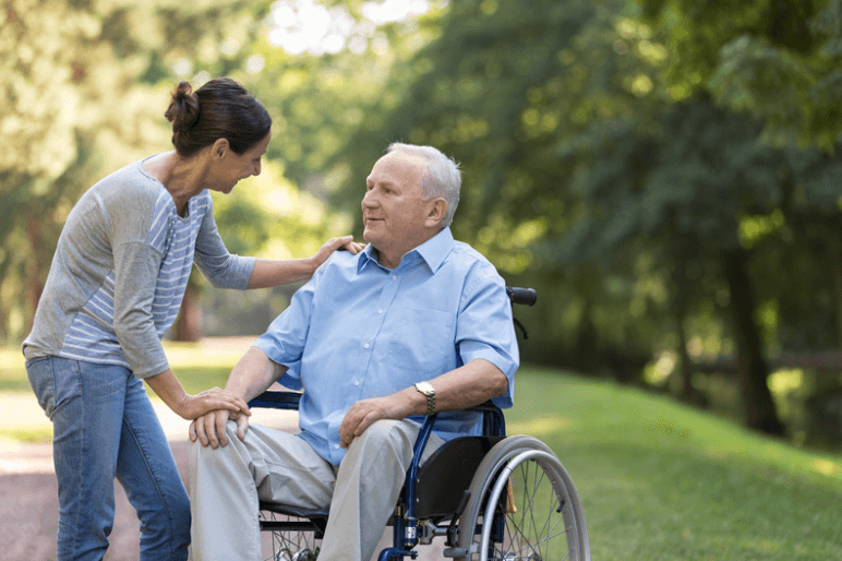 Volunteer woman assisting senior male resident in wheelchair outside in the garden at Kittson Healthcare. Both smiling and enjoying a cheerful moment together.