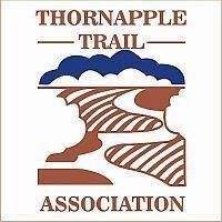 Paul Henry Thornapple Trail logo shows trail winding away in rust red, clouds in the background are blue.