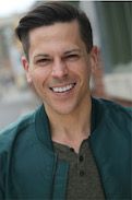 Stephen Drabicki, a man who is in his 30's and he is wearing a shirt with a dark green blazer, smiling widely at the camera.