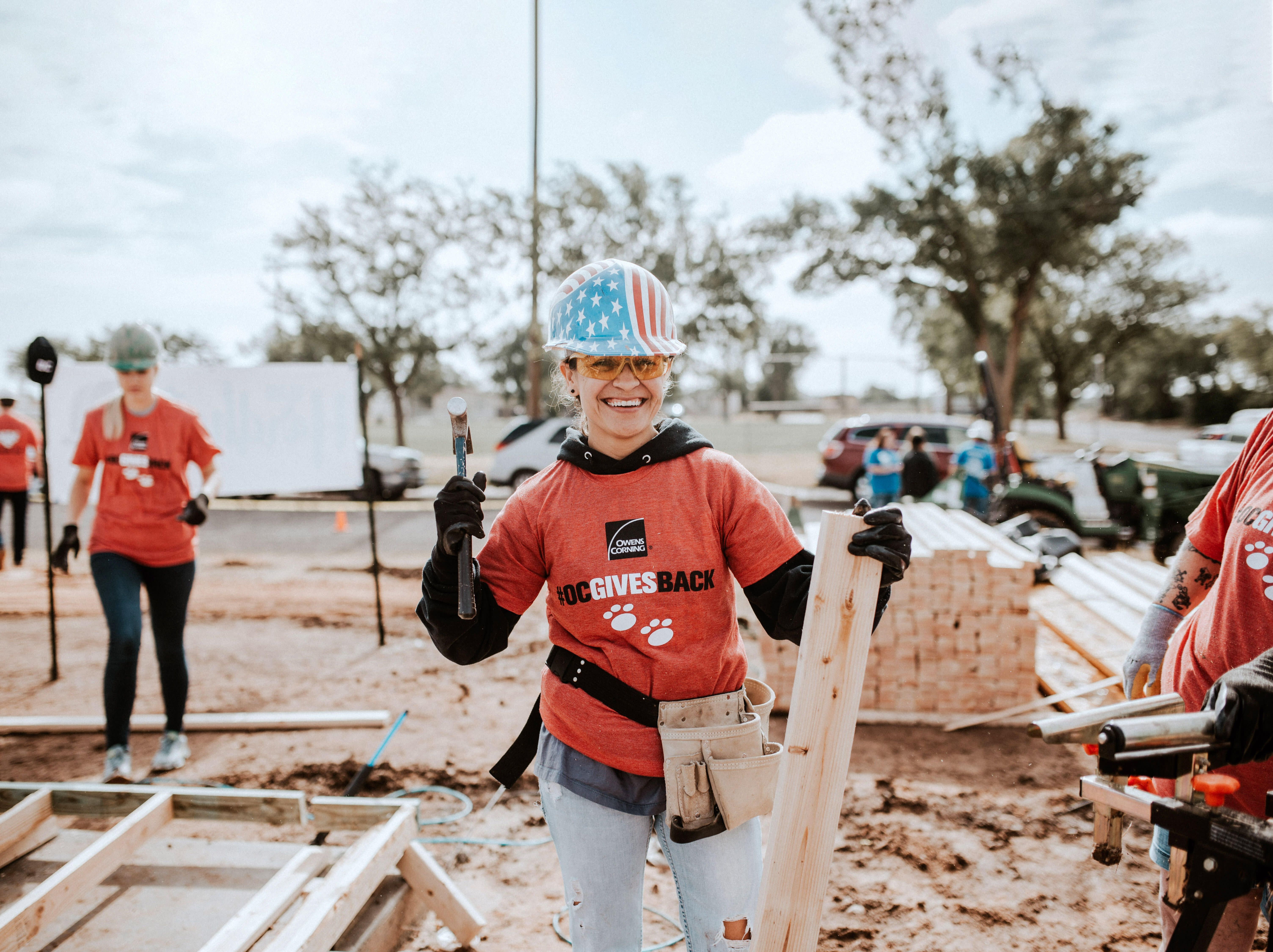 Close-up of a contractor using a nail gun to install shingles on a residential roof under clear blue skies, representing roof repair assistance for veterans.