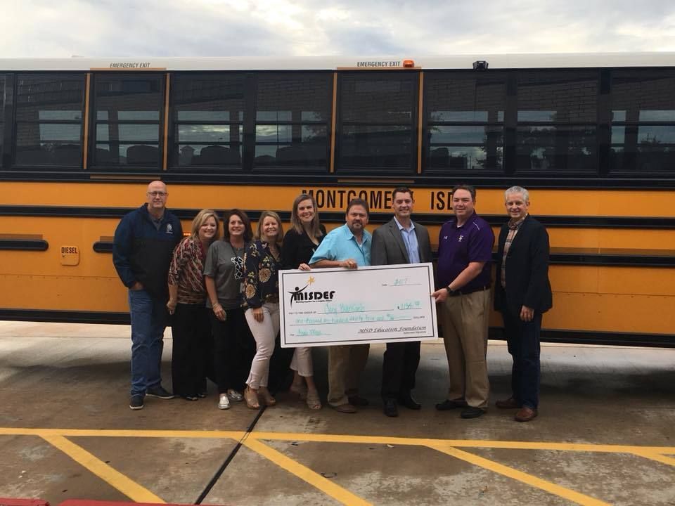 Group of people standing in front of a school bus with a big check.