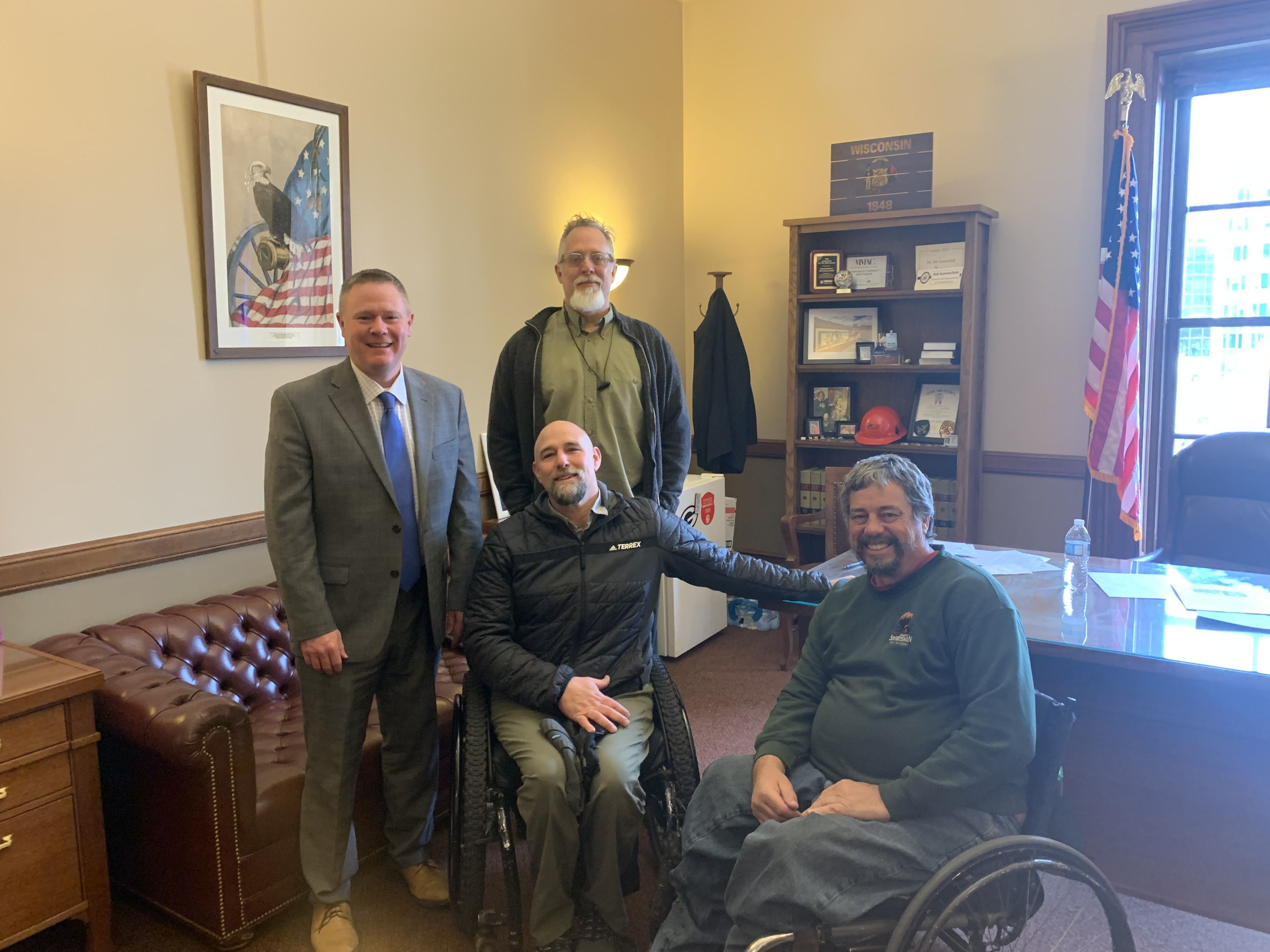 Four white men face the camera, two of the men are in wheelchairs