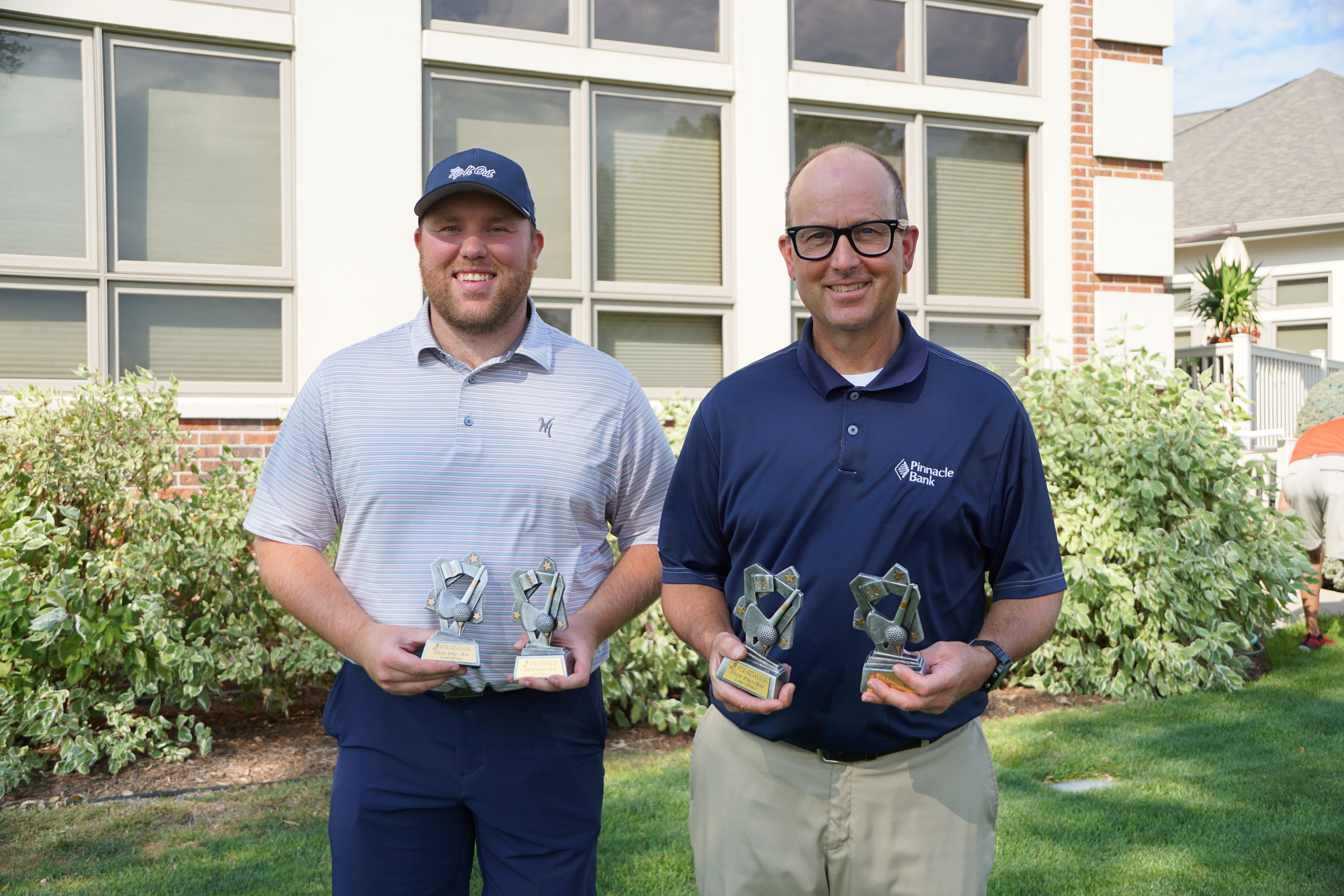 Two golfers holding tournament trophies.