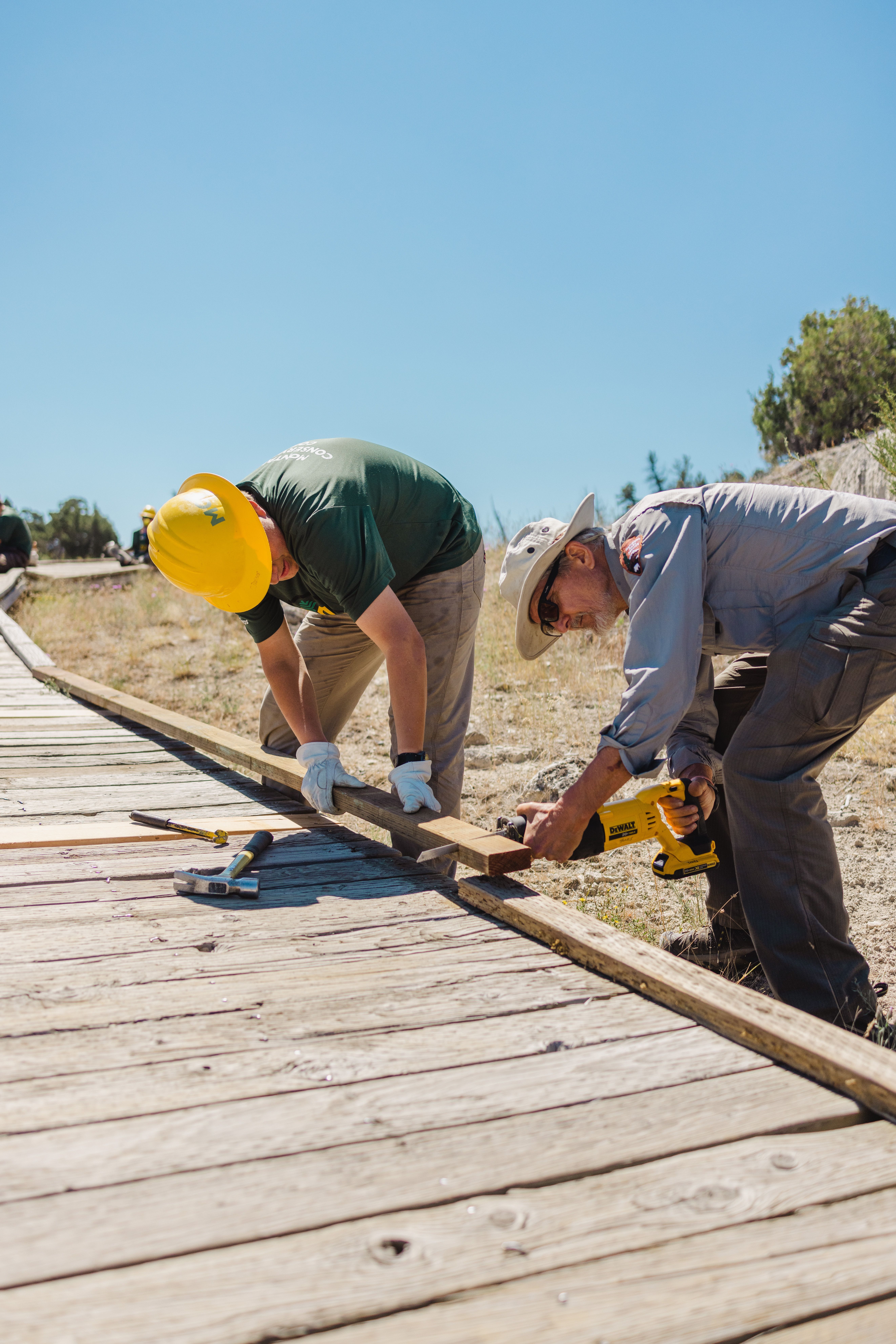 [Image Description: A youth crew participant and a National Park Service employee work side by side to replace a boardwalk plank.]