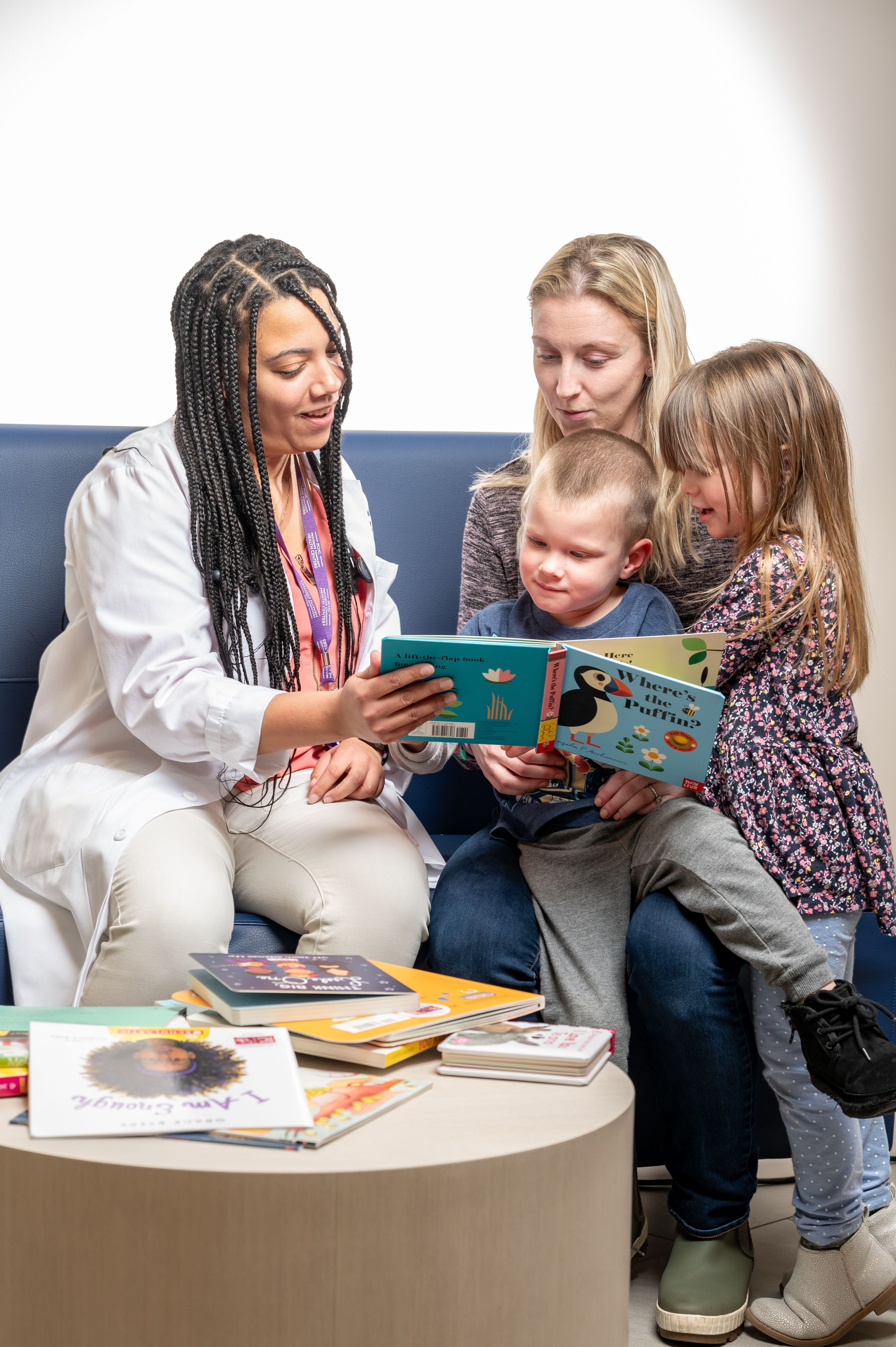 Pediatrician in long white coat hands book to family consisting of mother and two young children