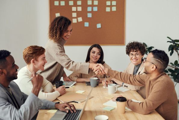 Group of people at a table and two of them are shaking hands.