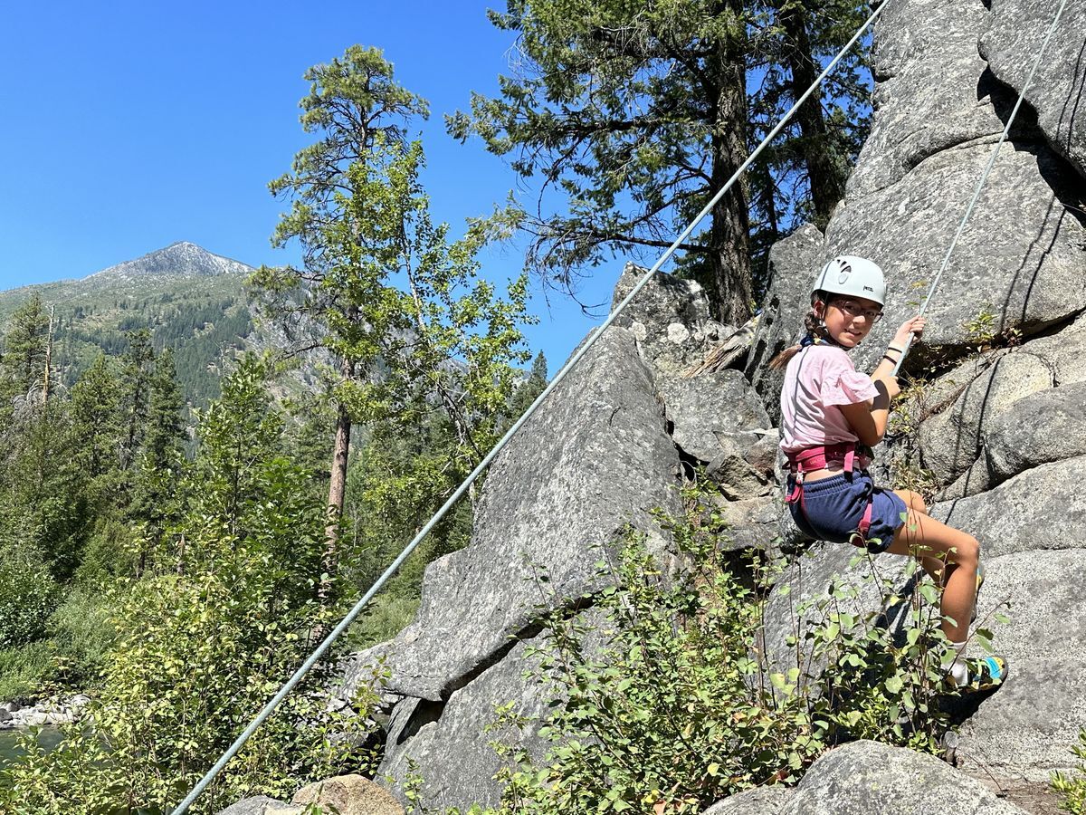 A student poses for the camera as she is climbing a rock face.