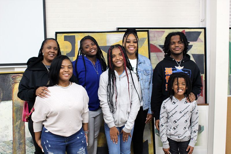 Aleasha and her family posing in front of a group of paintings.