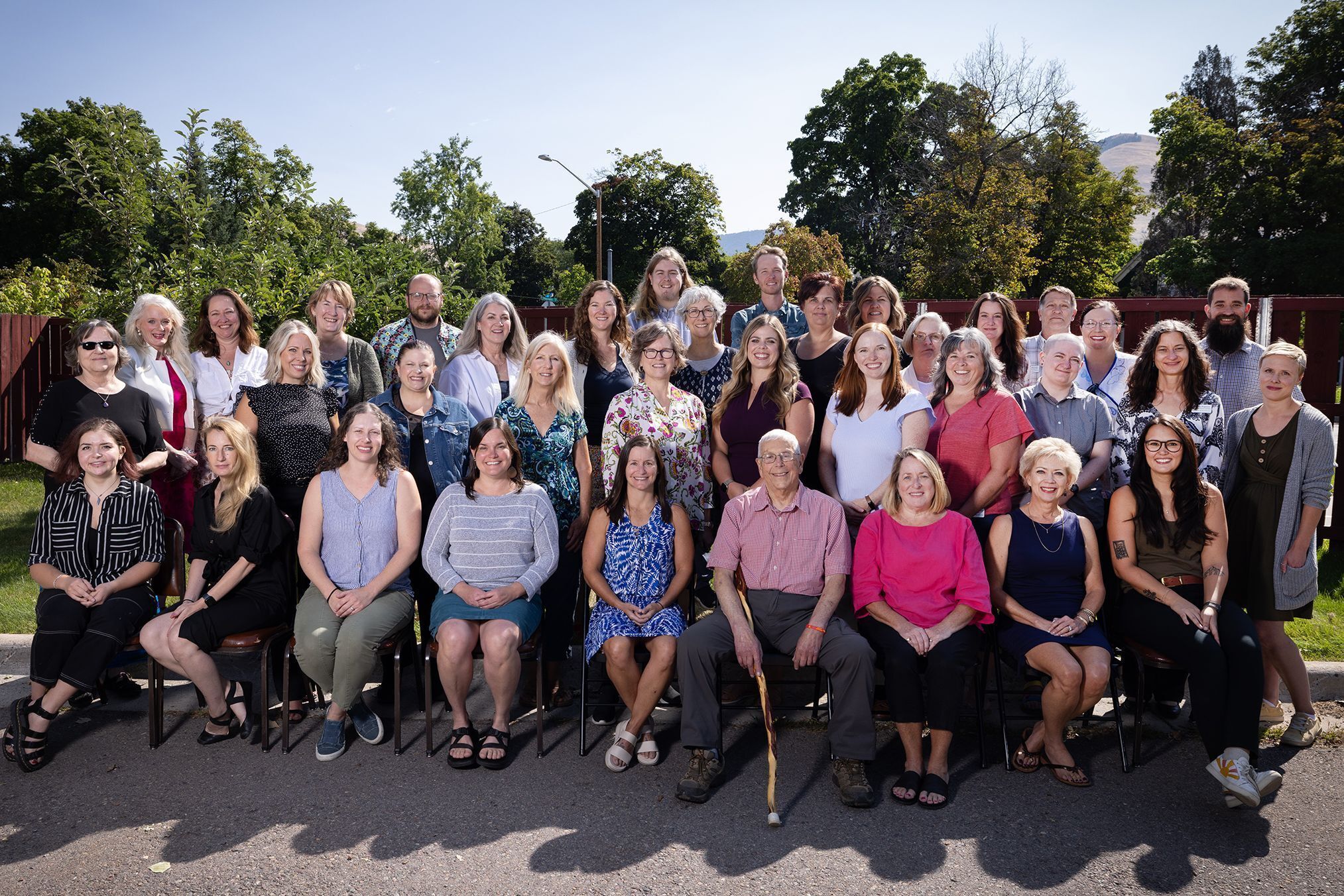 male and female staff standing and sitting together outside smiling for staff photo